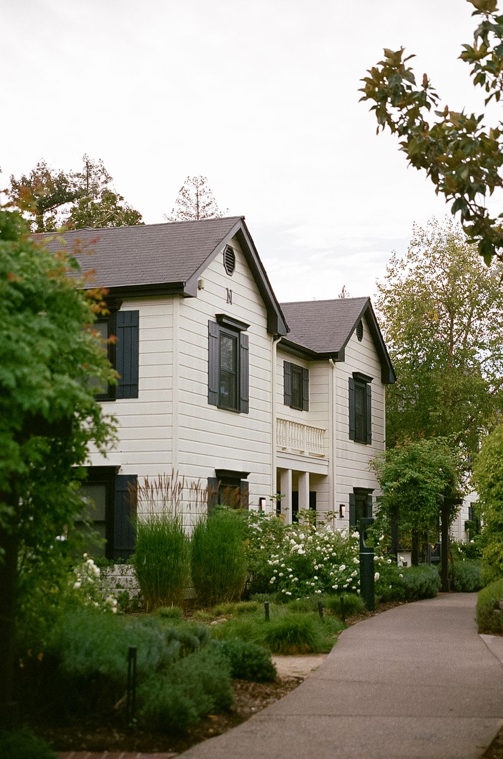 A white modern farmhouse-style building with black shutters and a landscaped garden path.