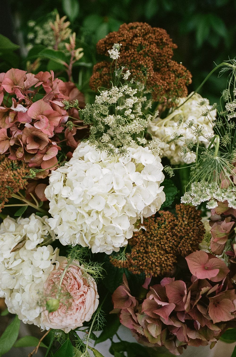 Beautiful floral arrangement featuring white hydrangeas, dusty pink roses, and dried brown sedum flowers.