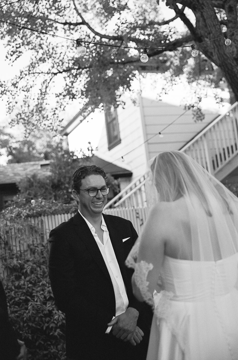 A wedding couple shares a joyful moment together outdoors under trees in black and white photography.