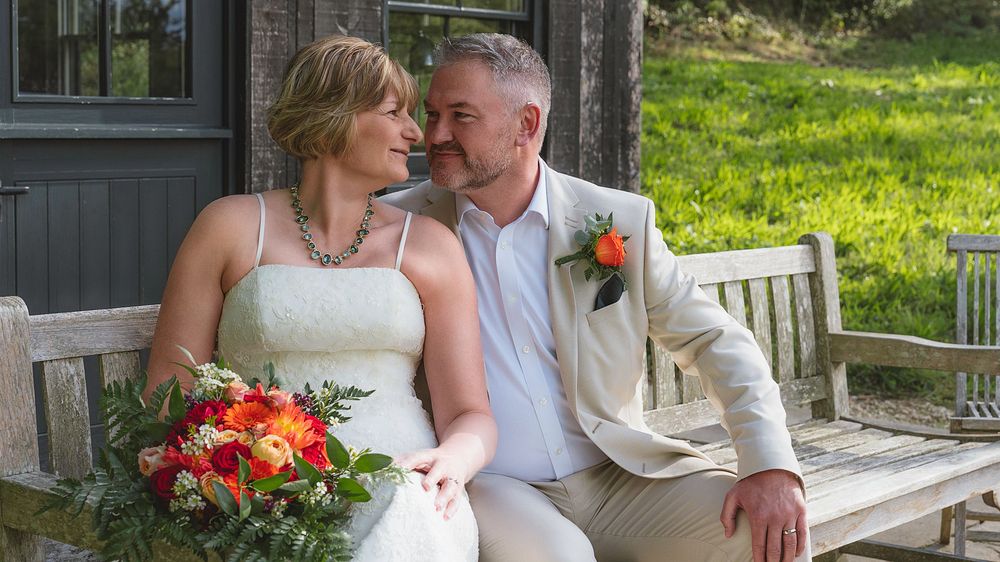 A romantic couple shares tender moments on a rustic bench surrounded by lush greenery and gardens.