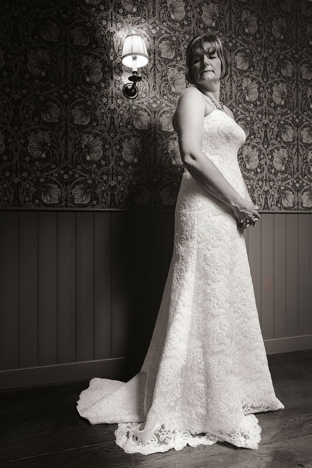 A series of black and white photos showing a flowing white lace wedding dress against a patterned wallpaper background.