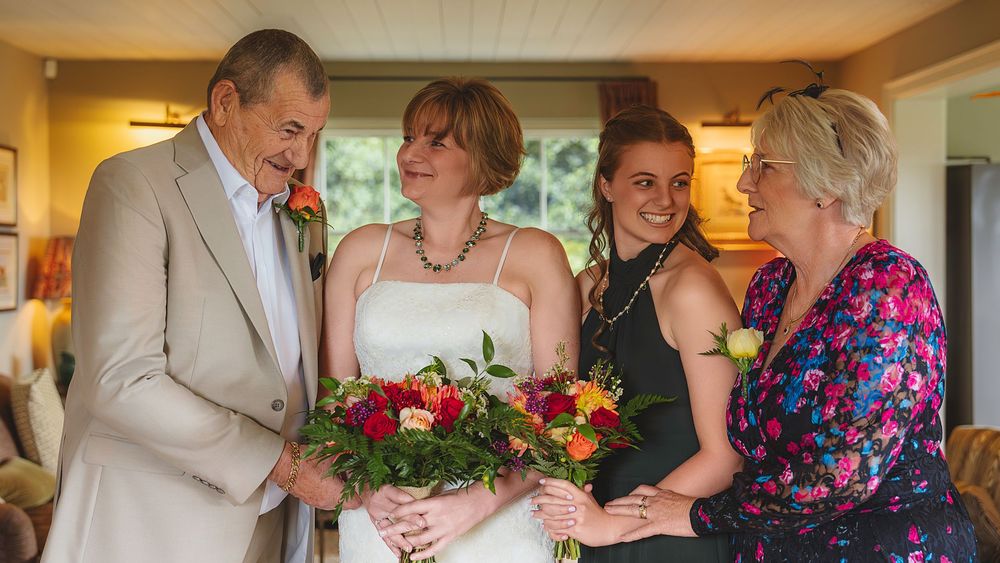 A group gathers around a vibrant floral bouquet in a warmly lit indoor setting during a special occasion.