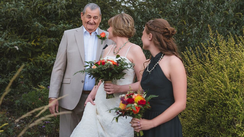 Wedding party poses for outdoor photos in a garden setting with bright floral bouquets and formal attire.