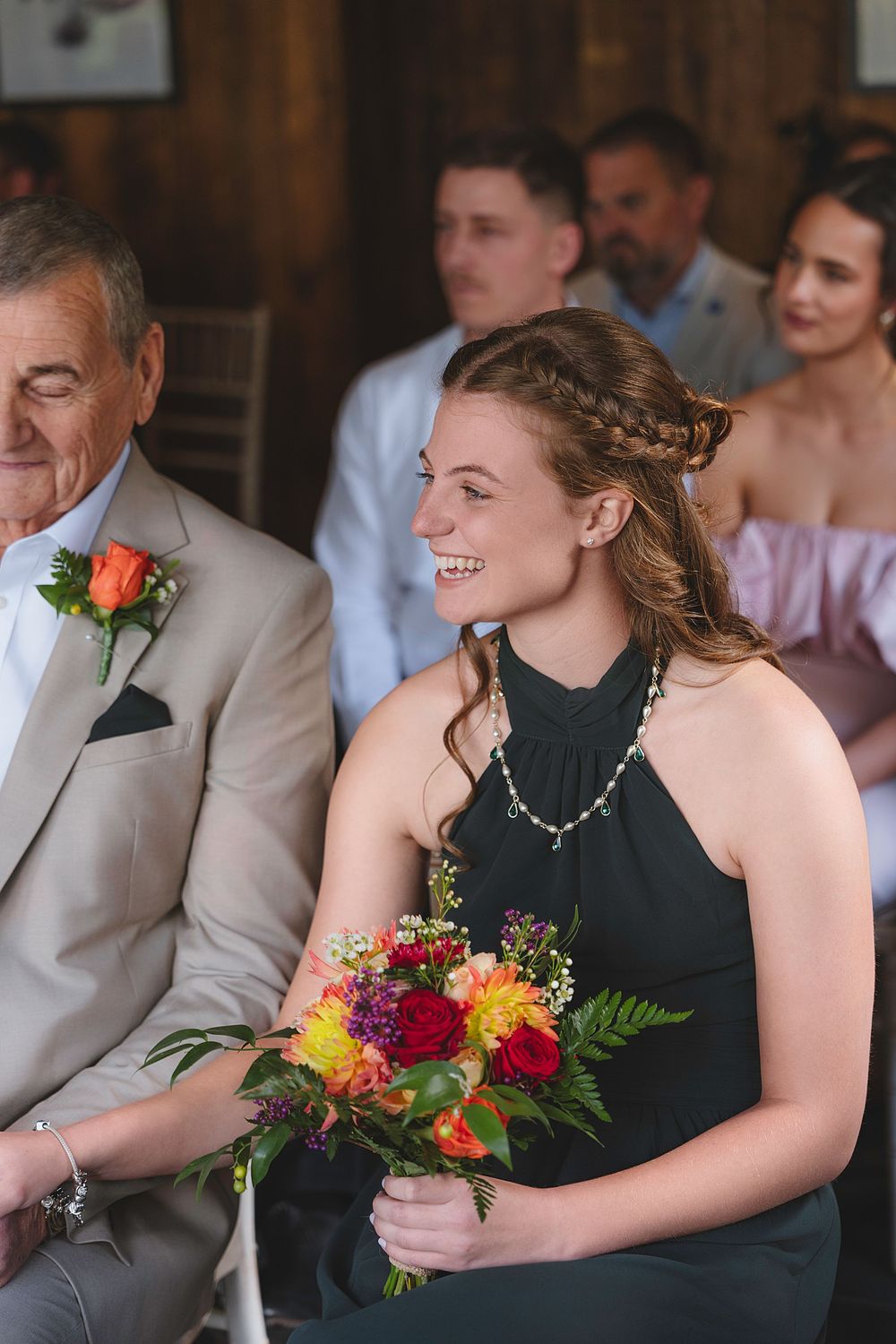 Bridesmaids in elegant black dresses hold vibrant autumn bouquets with orange and red flowers at a wedding ceremony.