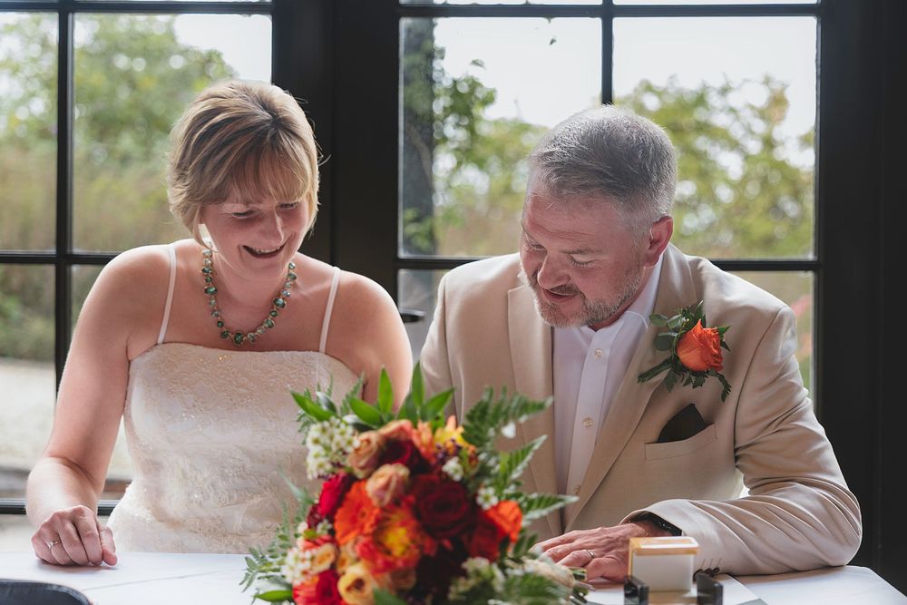 A couple signs their marriage documents at a table with a vibrant fall-colored floral arrangement.