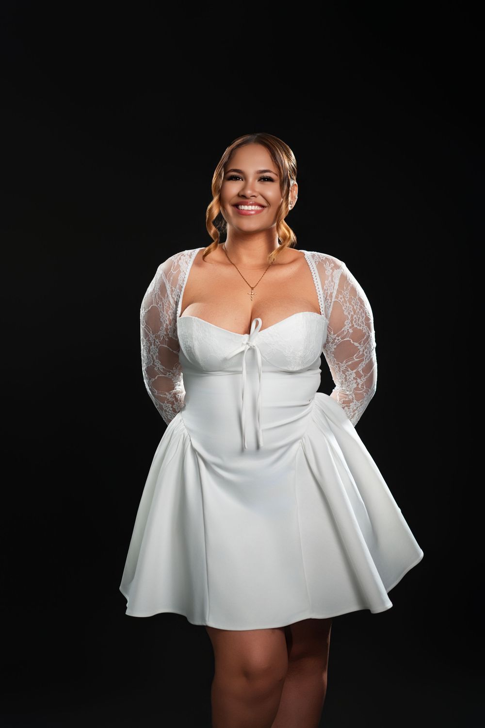 A model in a white lace mini dress with bell sleeves poses against a black background in a photo series.