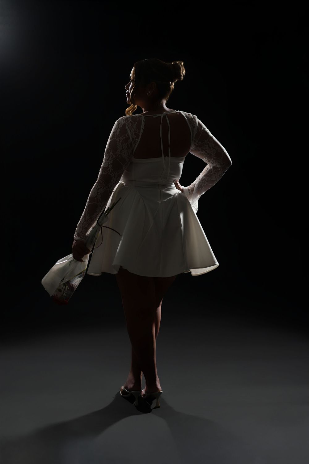 Silhouetted figure in a white vintage-style dress poses dramatically against dark background with rim lighting.