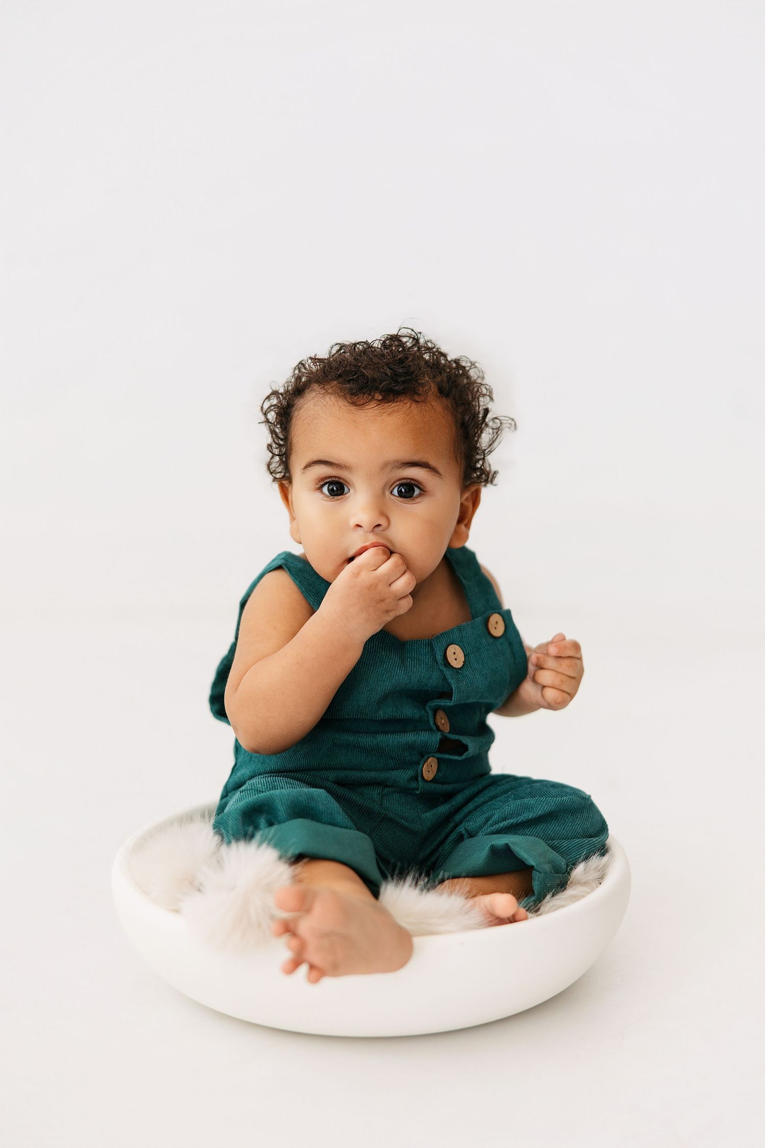 Small child in teal romper sits on white cushion in sequence of three adorable poses during photo session.