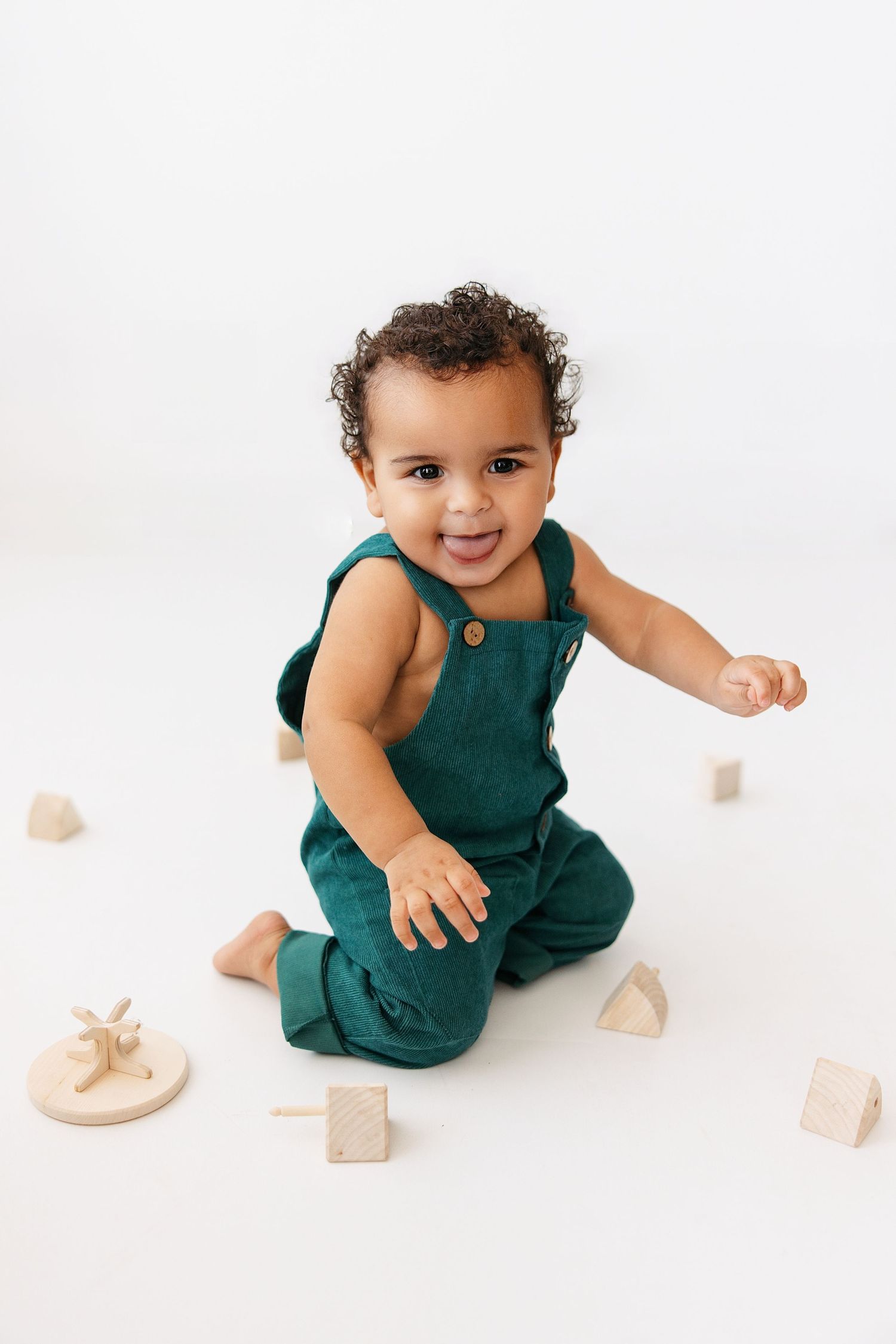 Baby in teal romper plays with wooden blocks during minimalist studio photo session.