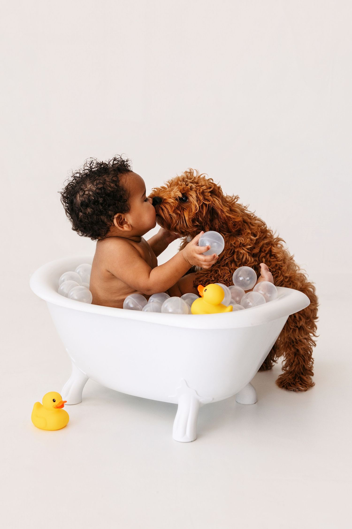 Baby taking a bath in white tub with rubber duck and bubbles, shown in three progressive playful poses.