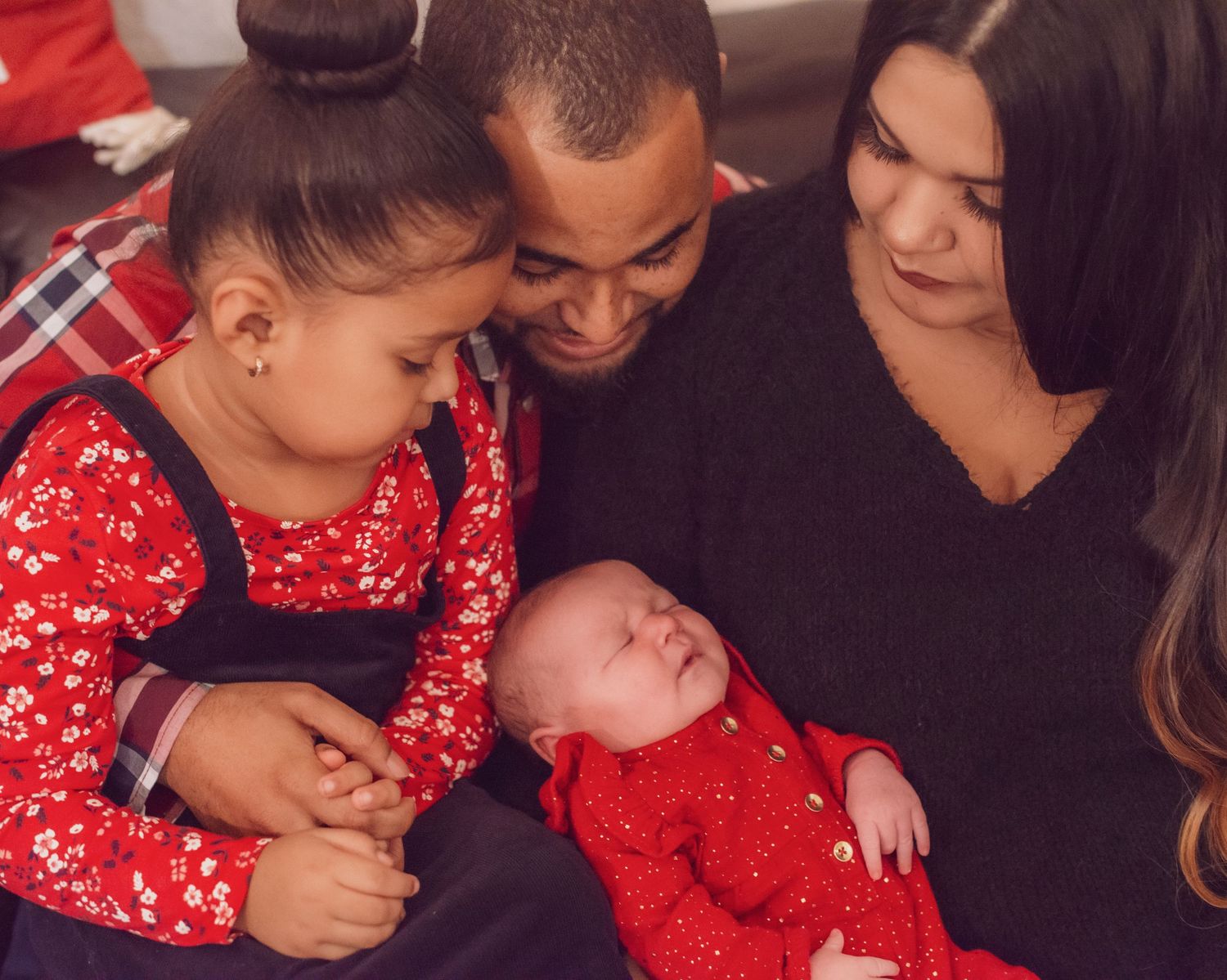 A family wearing red and black clothing sits together in a loving embrace during a holiday photo session.