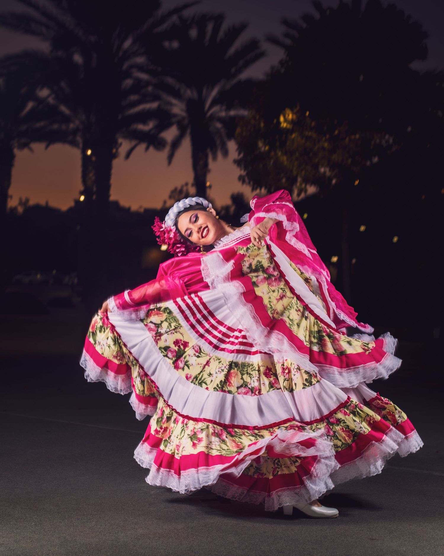 A dancer in a vibrant pink and white floral dress performs a traditional Mexican folklorico dance with flowing movements.