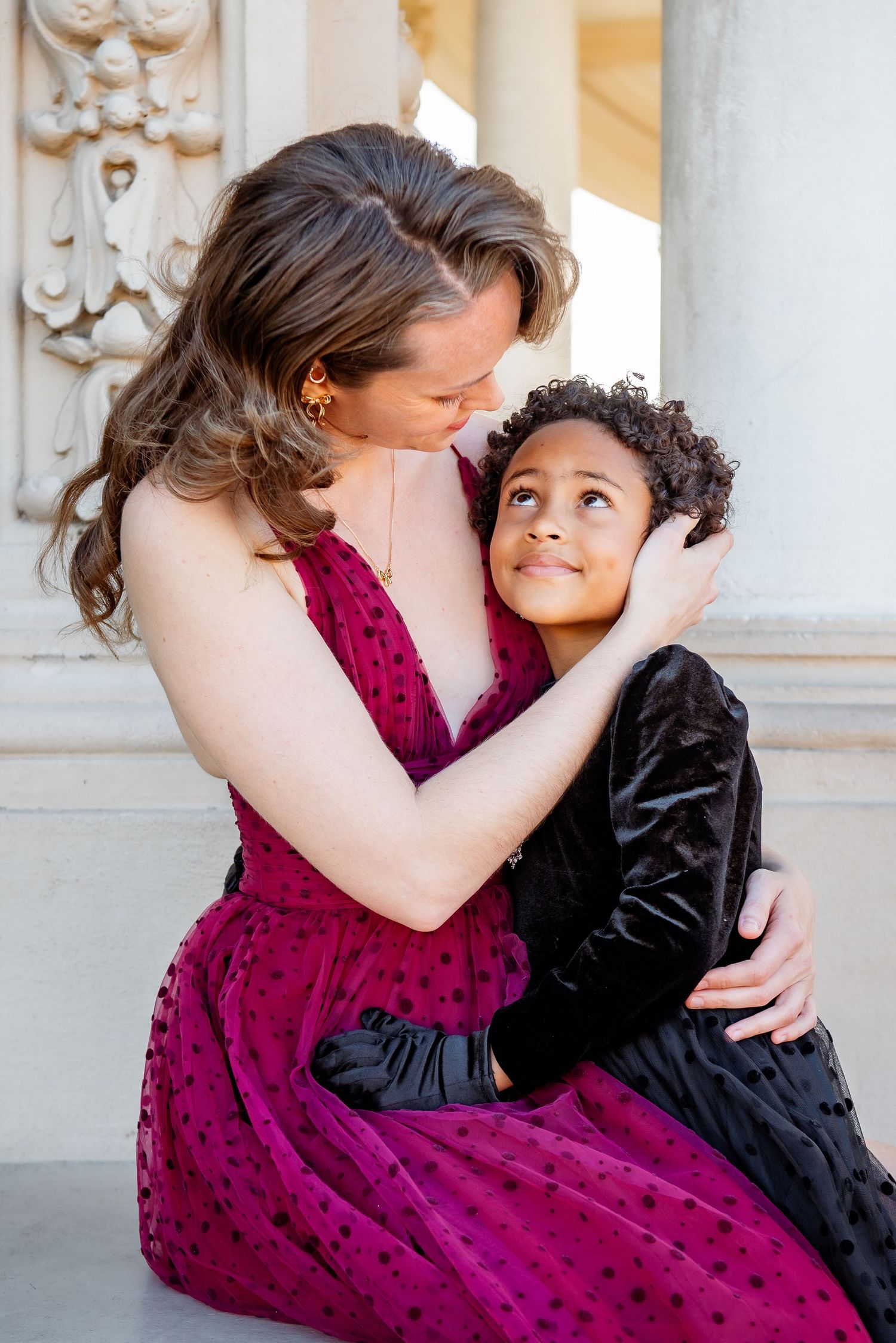 A sequence of tender moments showing a person in burgundy dress embracing another in black attire against an ornate wall.
