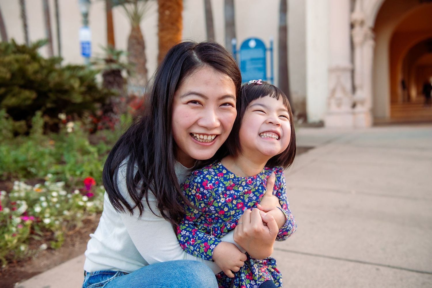 Two people sharing joyful moments together on a sidewalk with architectural elements in the background.