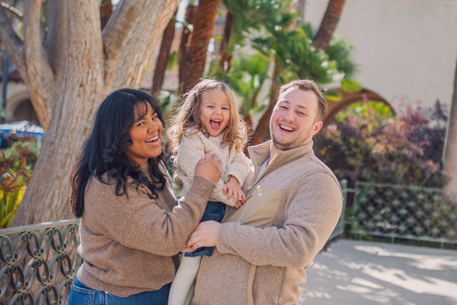 A group in matching beige sweaters laughs together while posing outdoors during a casual photo session.