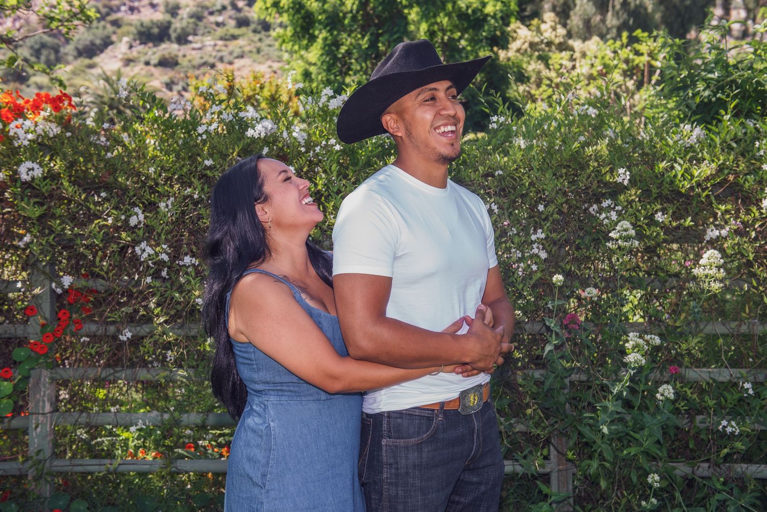 A couple shares a joyful moment while dancing together outdoors in a garden setting with blooming flowers.