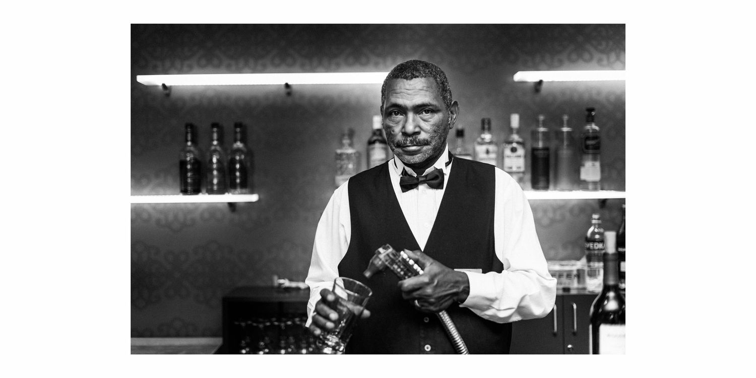 Black and white photo of bartender working behind an elegant bar counter.
