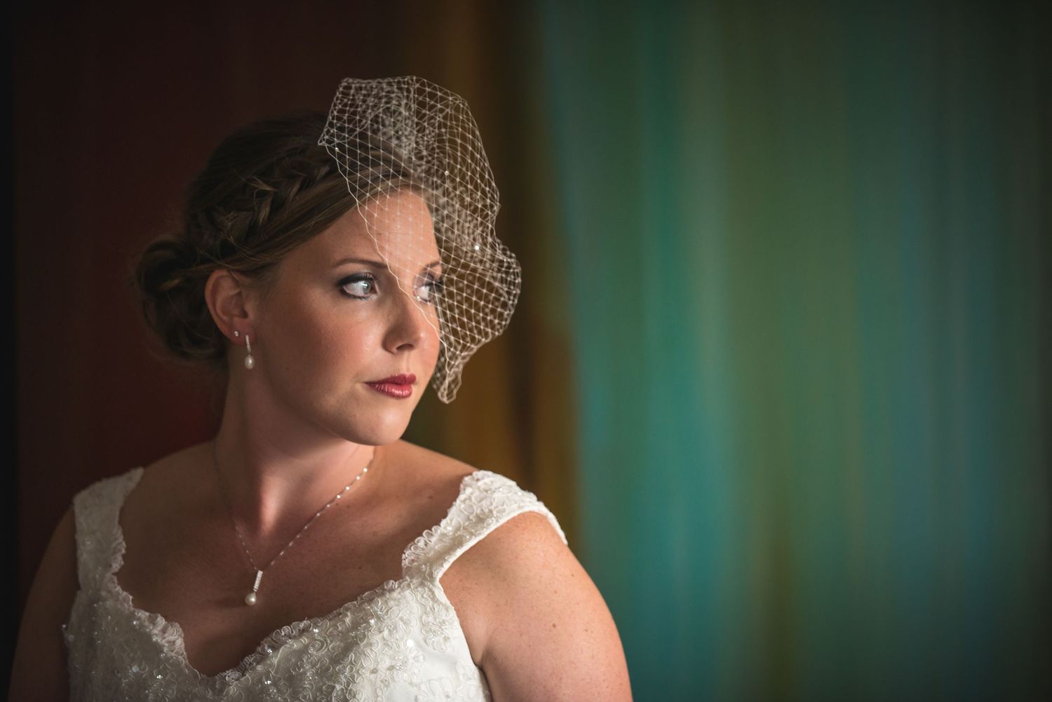 Vintage-inspired bridal portrait with birdcage veil against teal background.