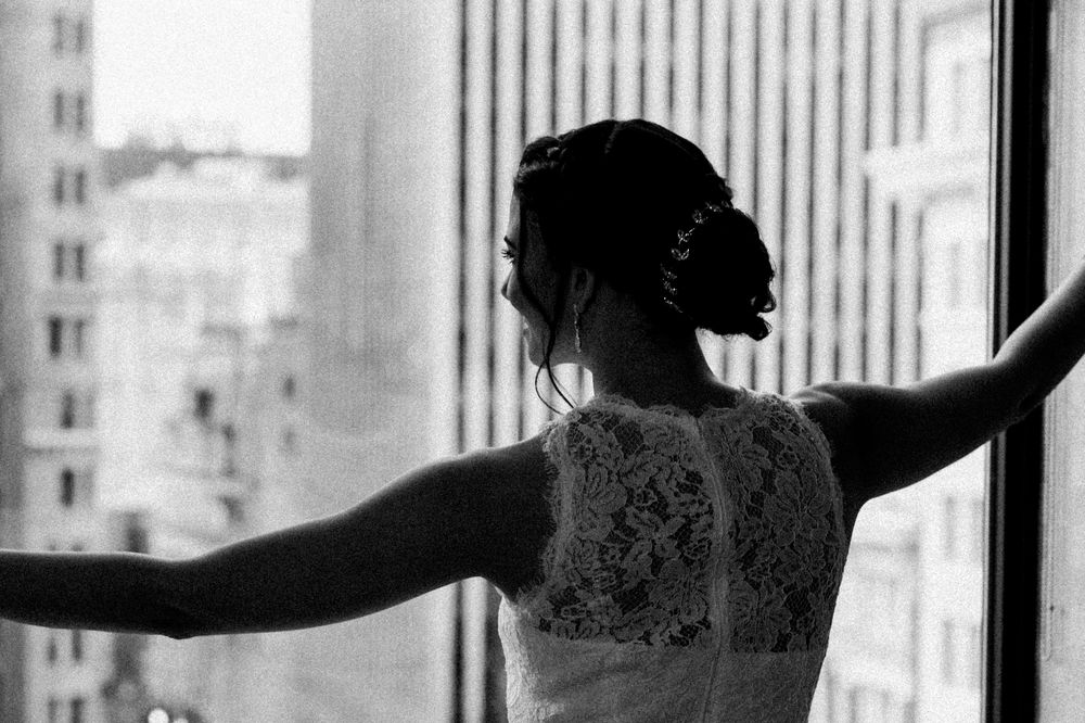 A silhouette of the bride in a lace dress with arms outstretched against a window.