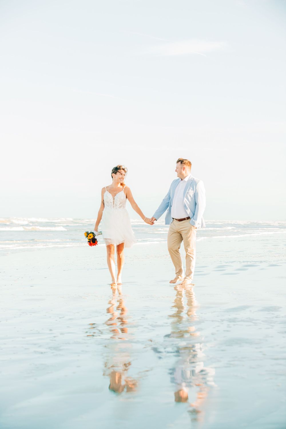 Sweet image of these two after exchanging vows at the beach along a serene beach shoreline in light pastel colors during sunset.