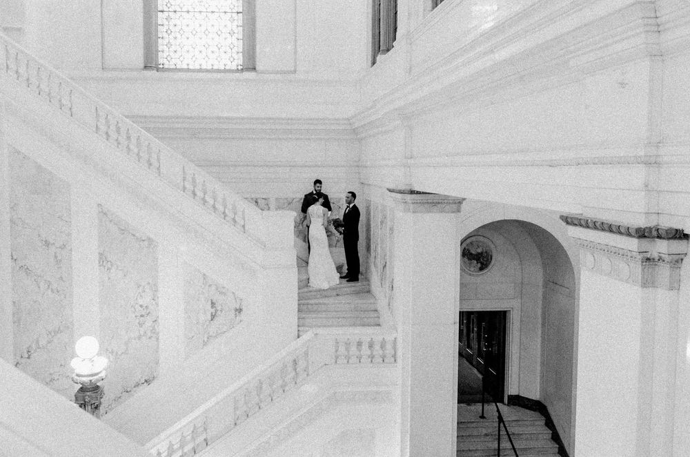 Bride and Groom exchanging vows on their wedding day standing on a white marble staircase in an elegant hotel.