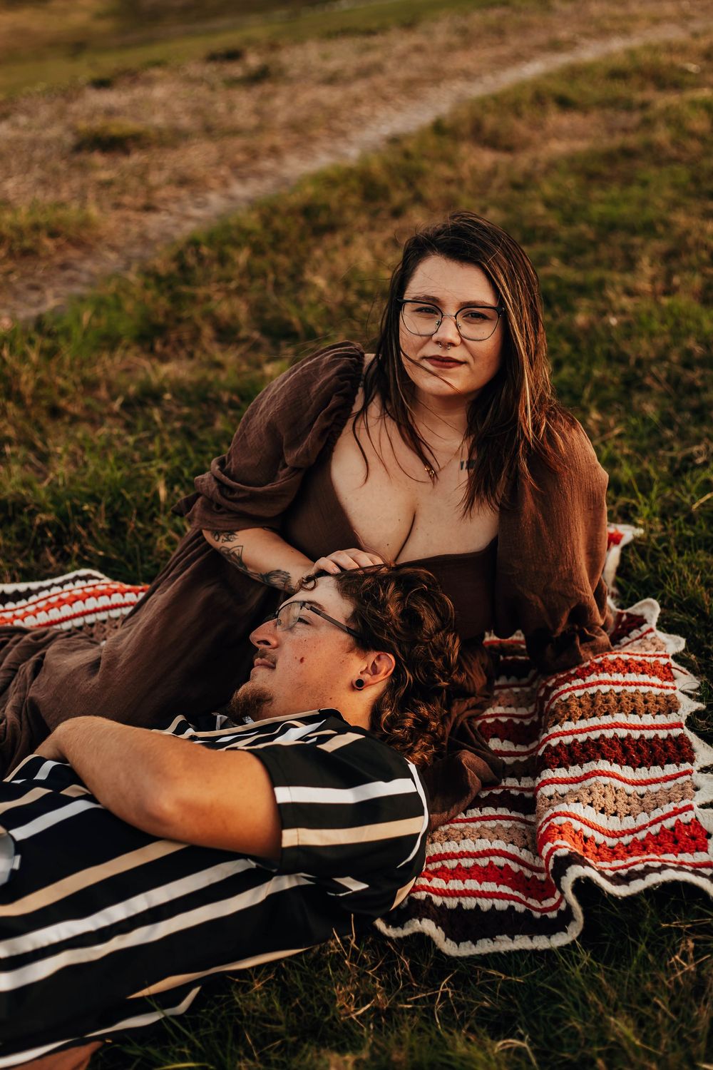 A couple lying on a striped blanket sharing an intimate moment in golden sunlight.