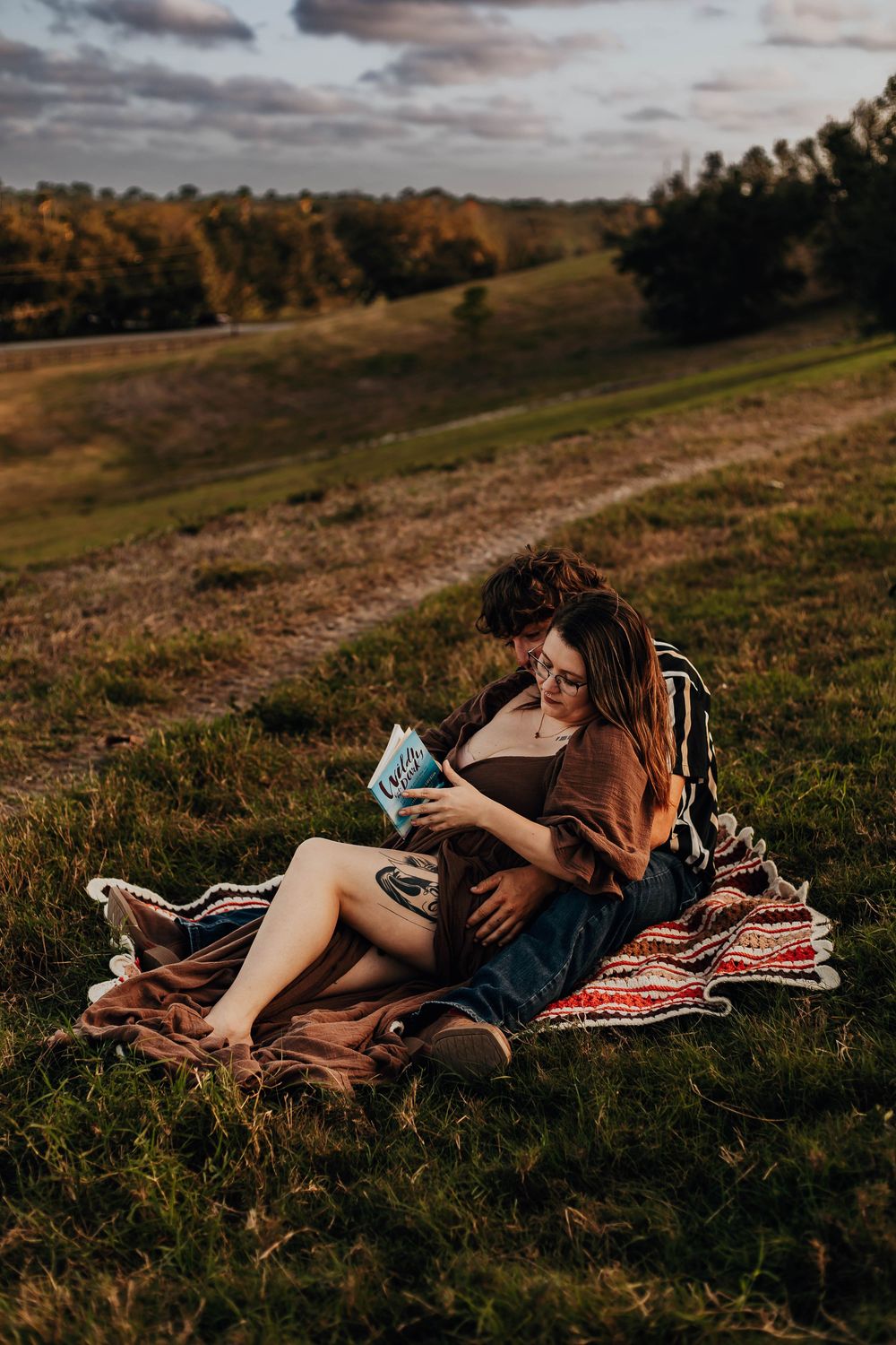 A cozy outdoor reading scene on a blanket during golden hour with rolling hills and autumn trees in the background.