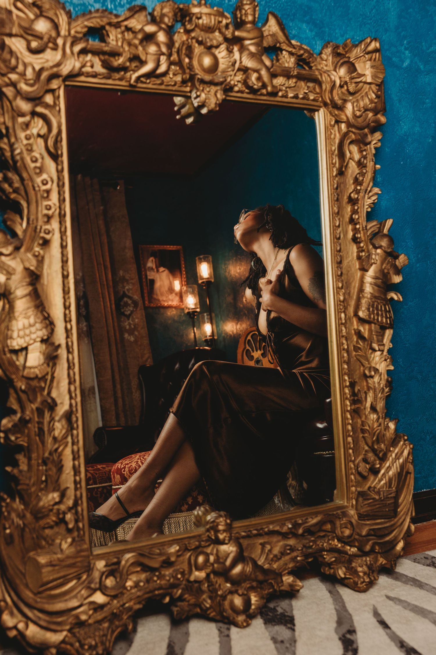 Ornate gold baroque mirror frames displayed in sequence against a blue wall with moody candlelit reflections.