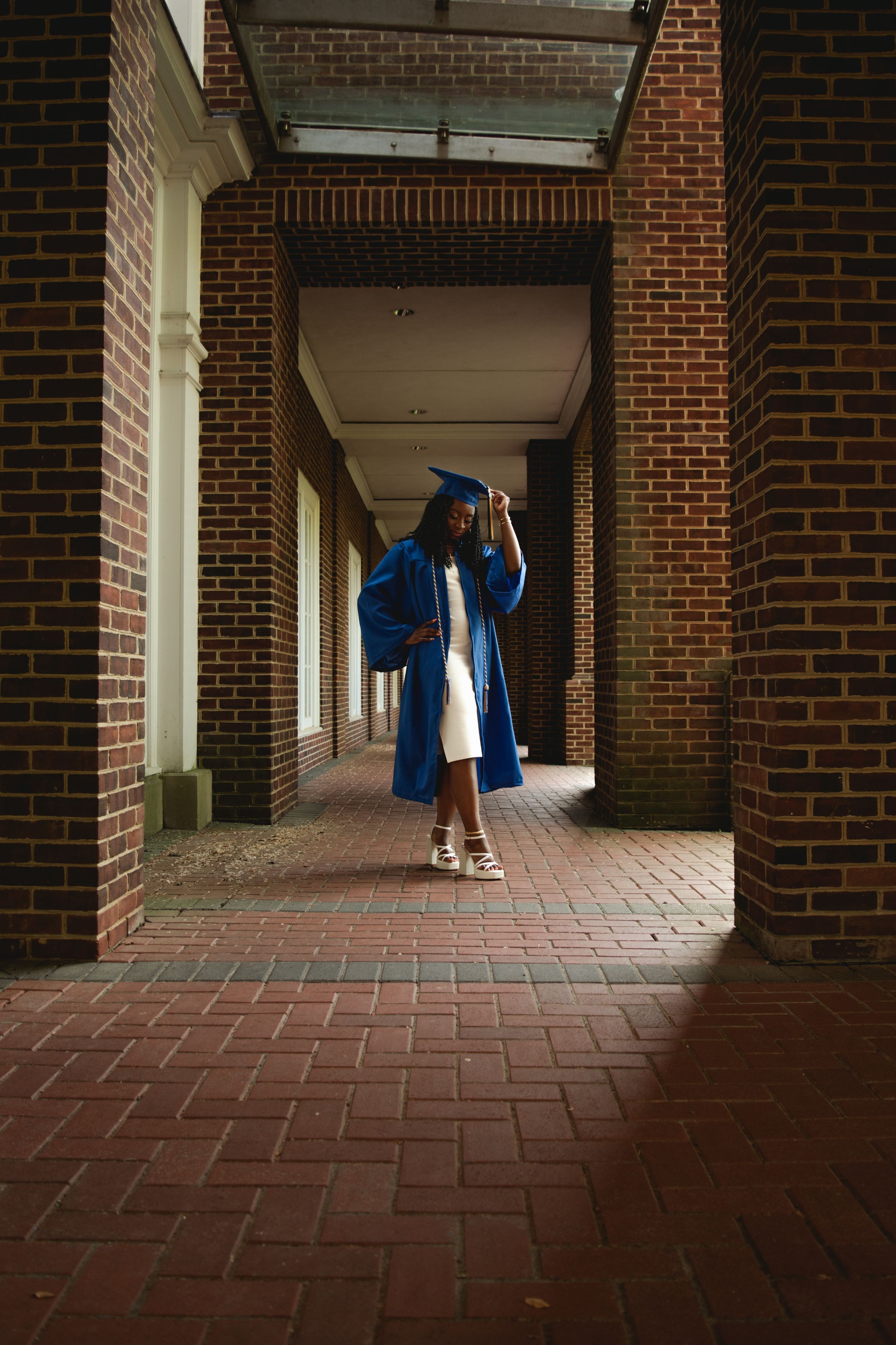 A series of brick archways with red tiled floors creates a dramatic hallway perspective with blue graduation robes visible.