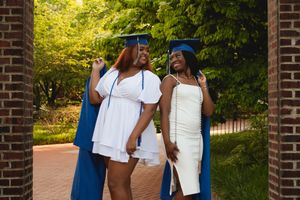 Wedding party in blue and white attire walks along a brick-lined pathway surrounded by lush greenery.