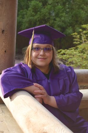 Graduate in purple cap and gown resting on wooden railing during outdoor photo session.