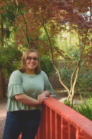 Person in mint green top posing by red railing in garden setting with autumn foliage.