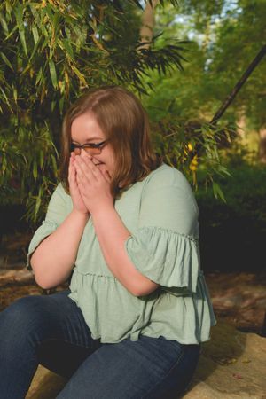 A person in a mint green top and jeans sits outdoors covering their face with their hands in a sequence of photos.