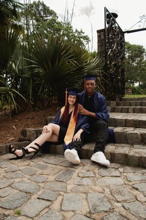 A graduation photoshoot sequence showing someone in a blue cap and gown sitting on stone steps near tropical plants.