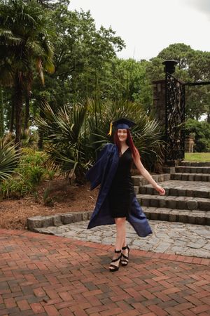 Graduate in blue cap and gown poses on brick walkway near tropical landscaping in series of celebratory shots.