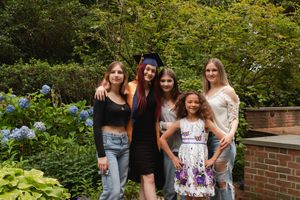 A group of friends pose together in a garden with blooming hydrangeas and greenery against a brick wall.
