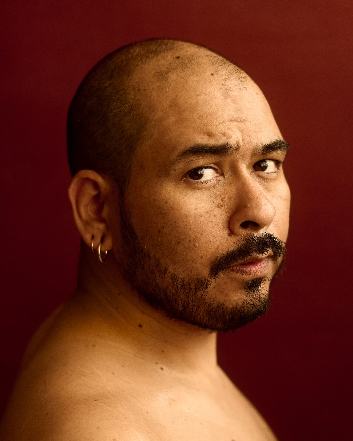 Close-up portrait of tattooed man with beard wearing bracelets and ring in dramatic lighting.