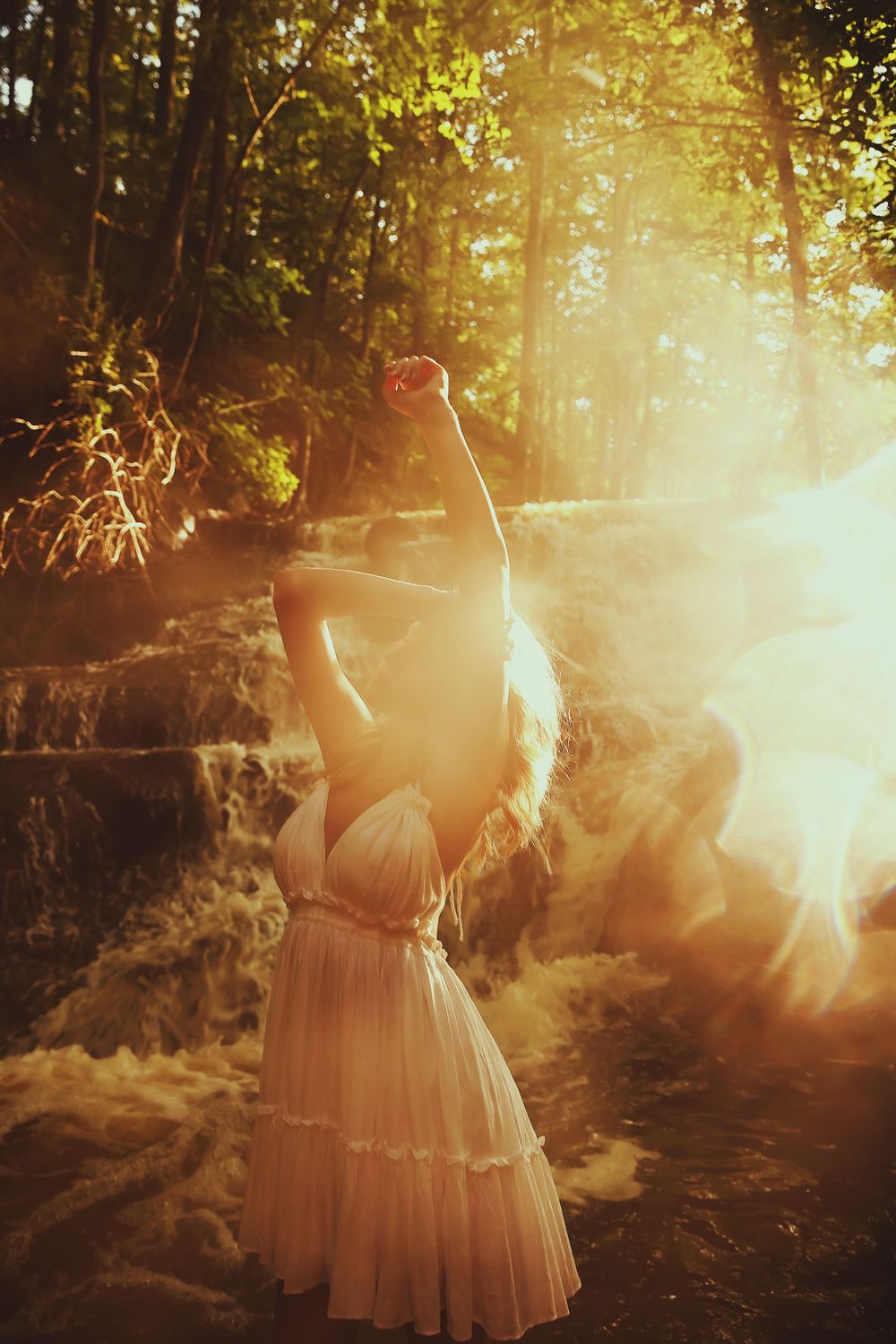 A dreamy forest scene with sunlight streaming through trees illuminating a figure in a flowing white dress.