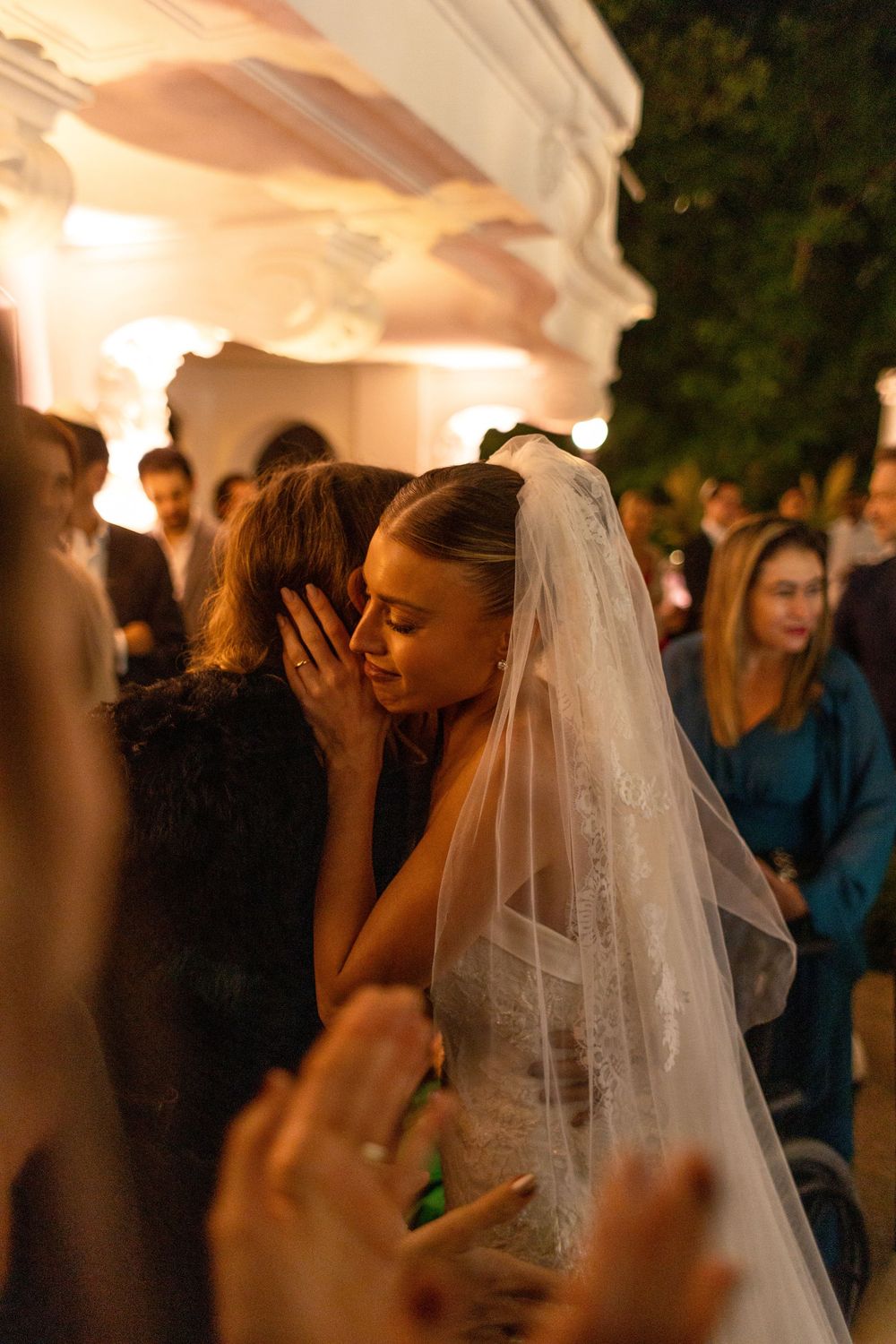 Wedding celebration under warm lighting with a bride in white dress and veil among guests.