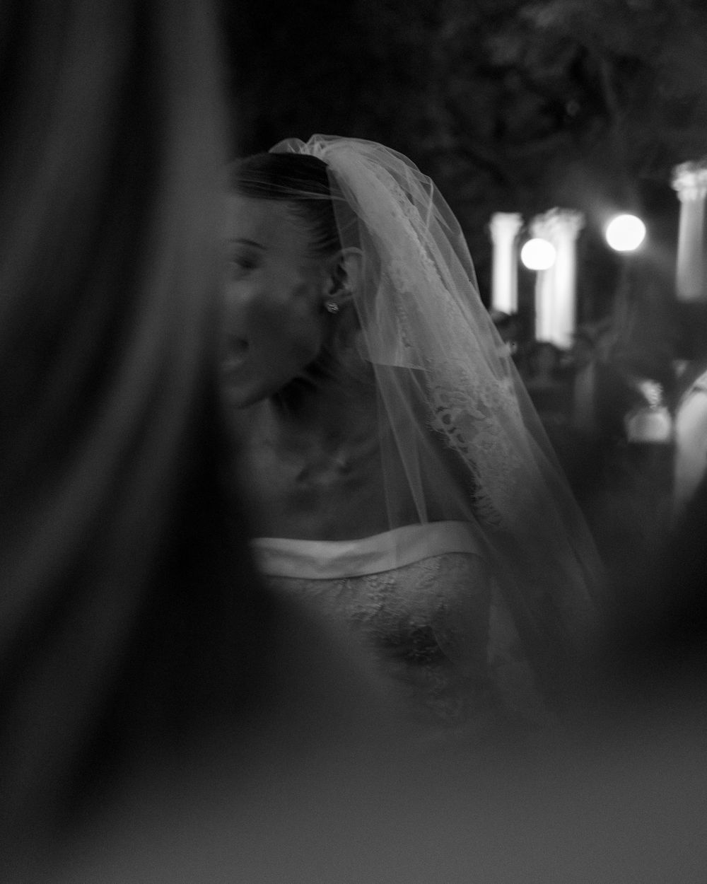 An artistic black and white portrait of a bride wearing a delicate veil in soft evening light.