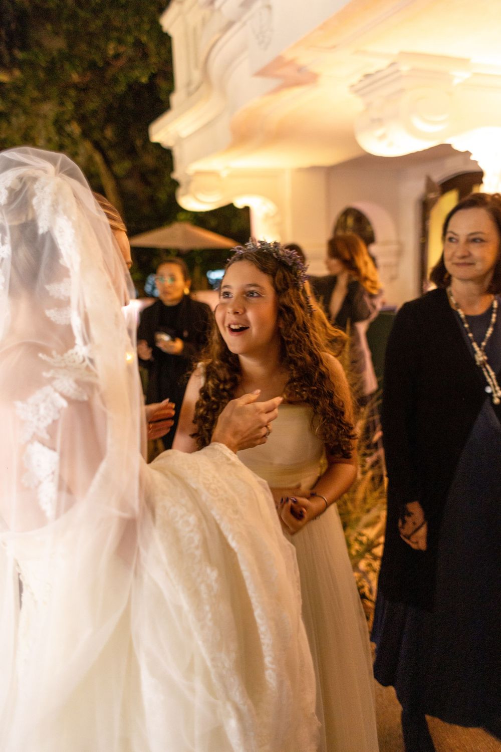 Guests in formal attire mingle at an elegant evening wedding reception with warm lighting and white decor.