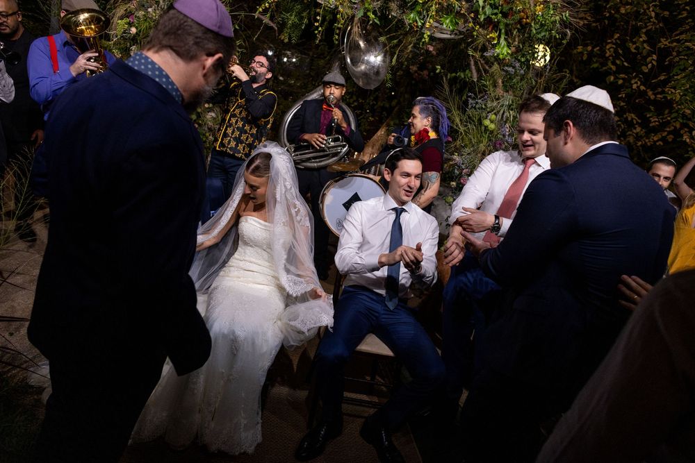 Wedding guests dance and celebrate at an outdoor evening reception under string lights.