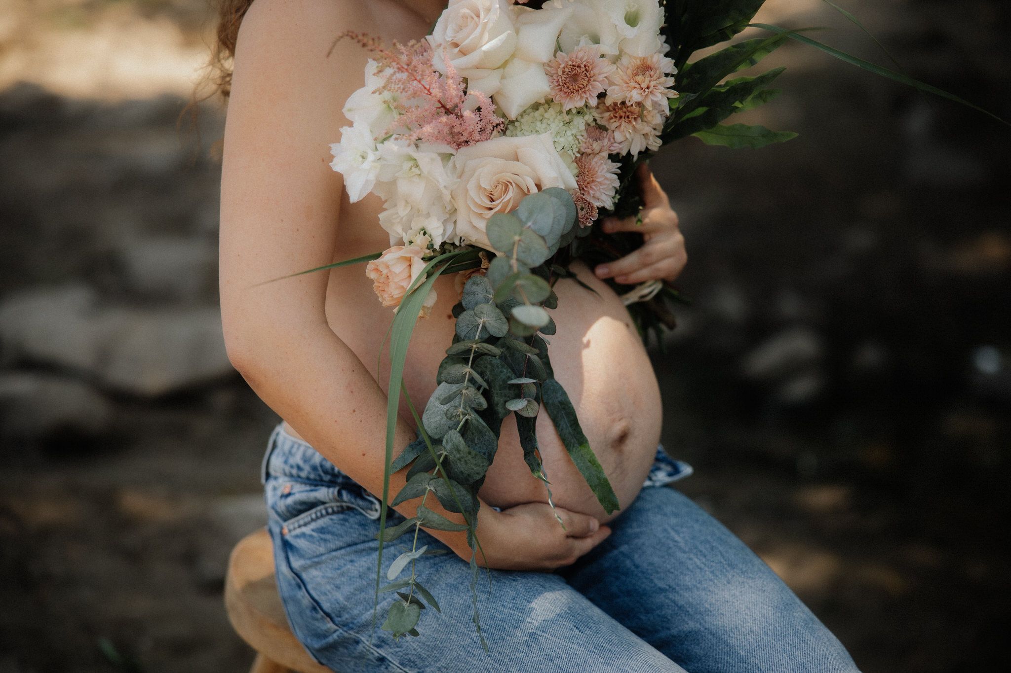 A person in jeans holds a delicate pink and white floral bouquet against a dark outdoor background.