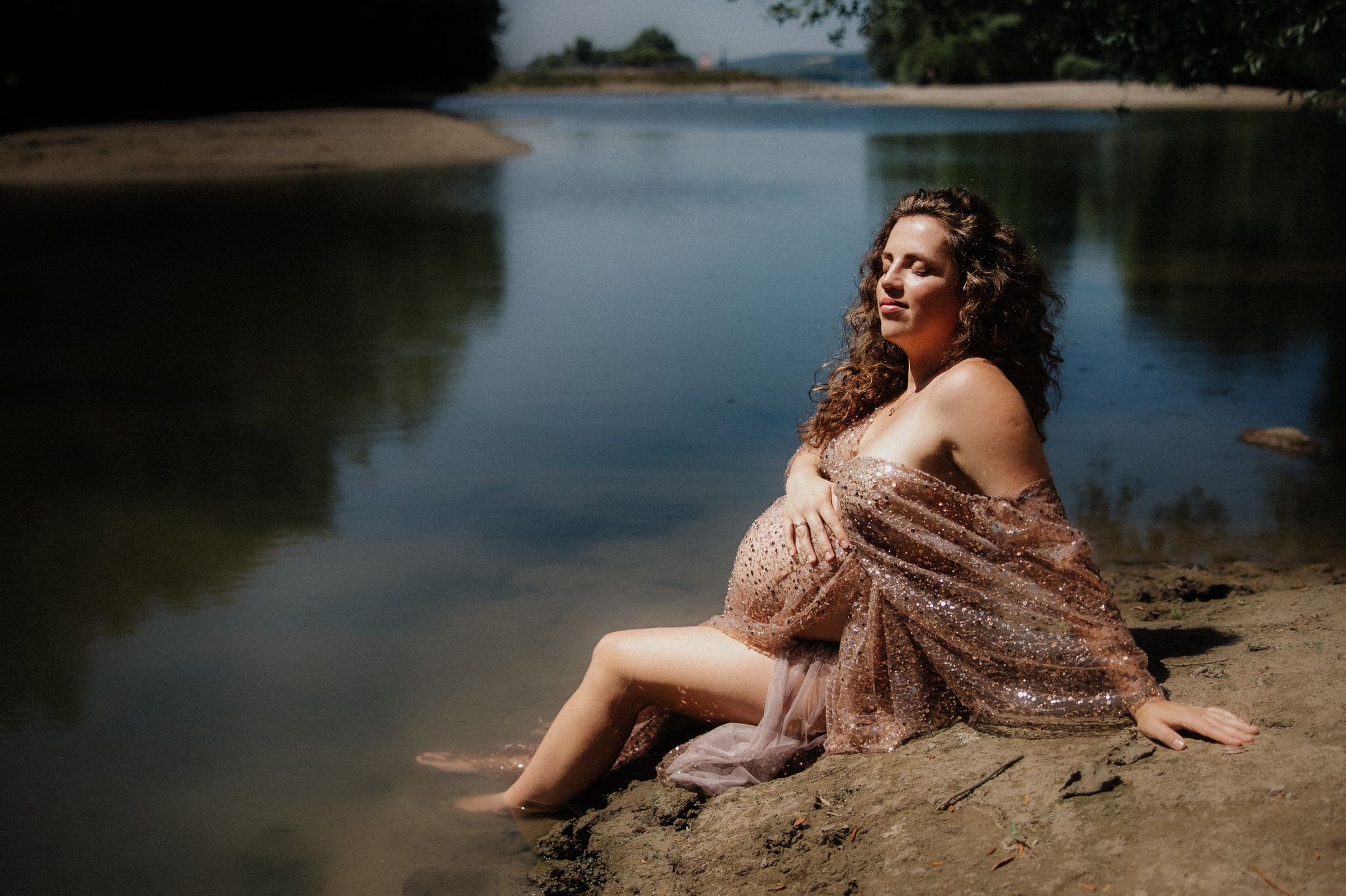 A model in a sequined dress poses gracefully on a sandy beach near calm waters during a sunset photoshoot.
