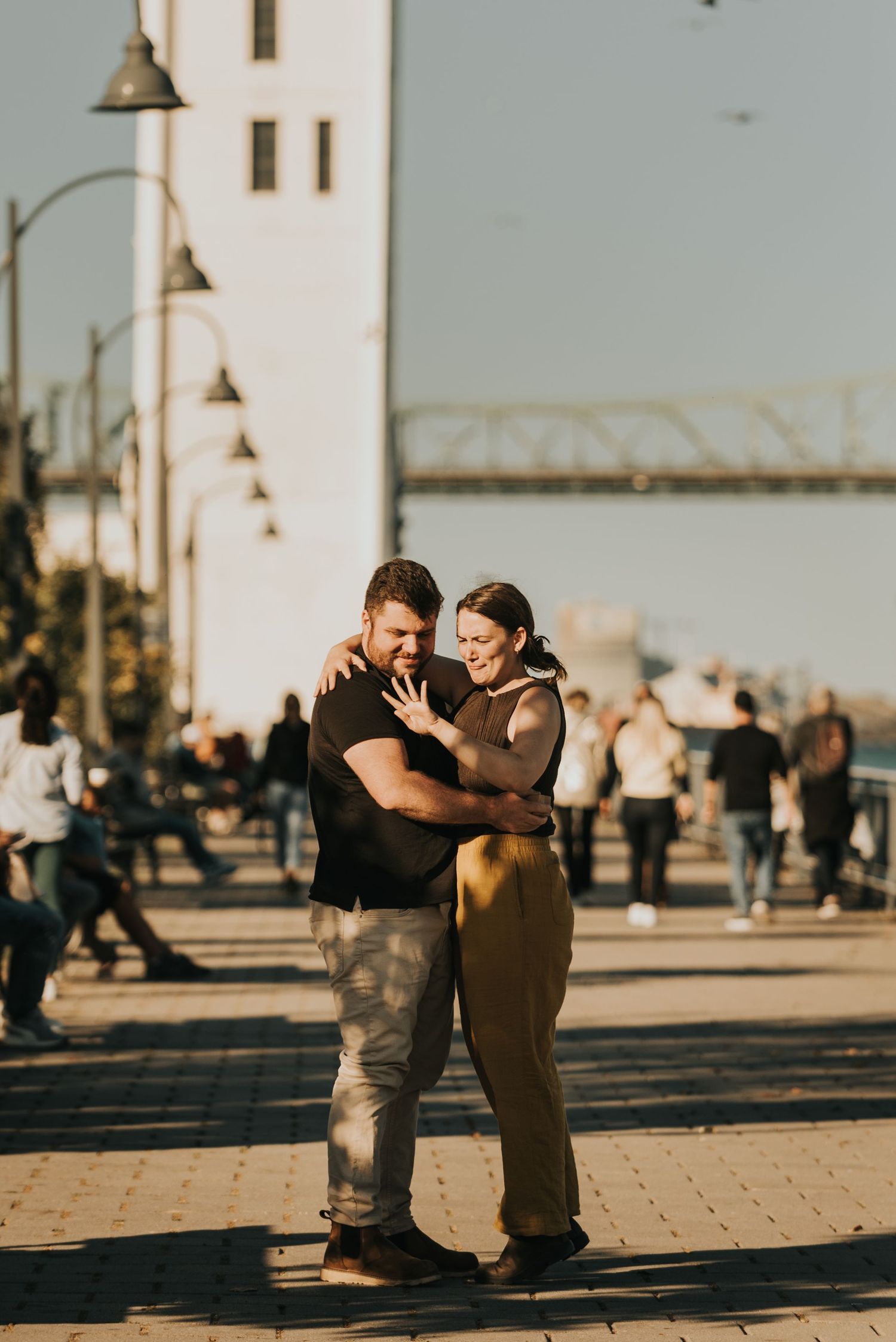 A couple embraces during a romantic sunset photoshoot on a brick-paved boardwalk with lamp posts in the background.