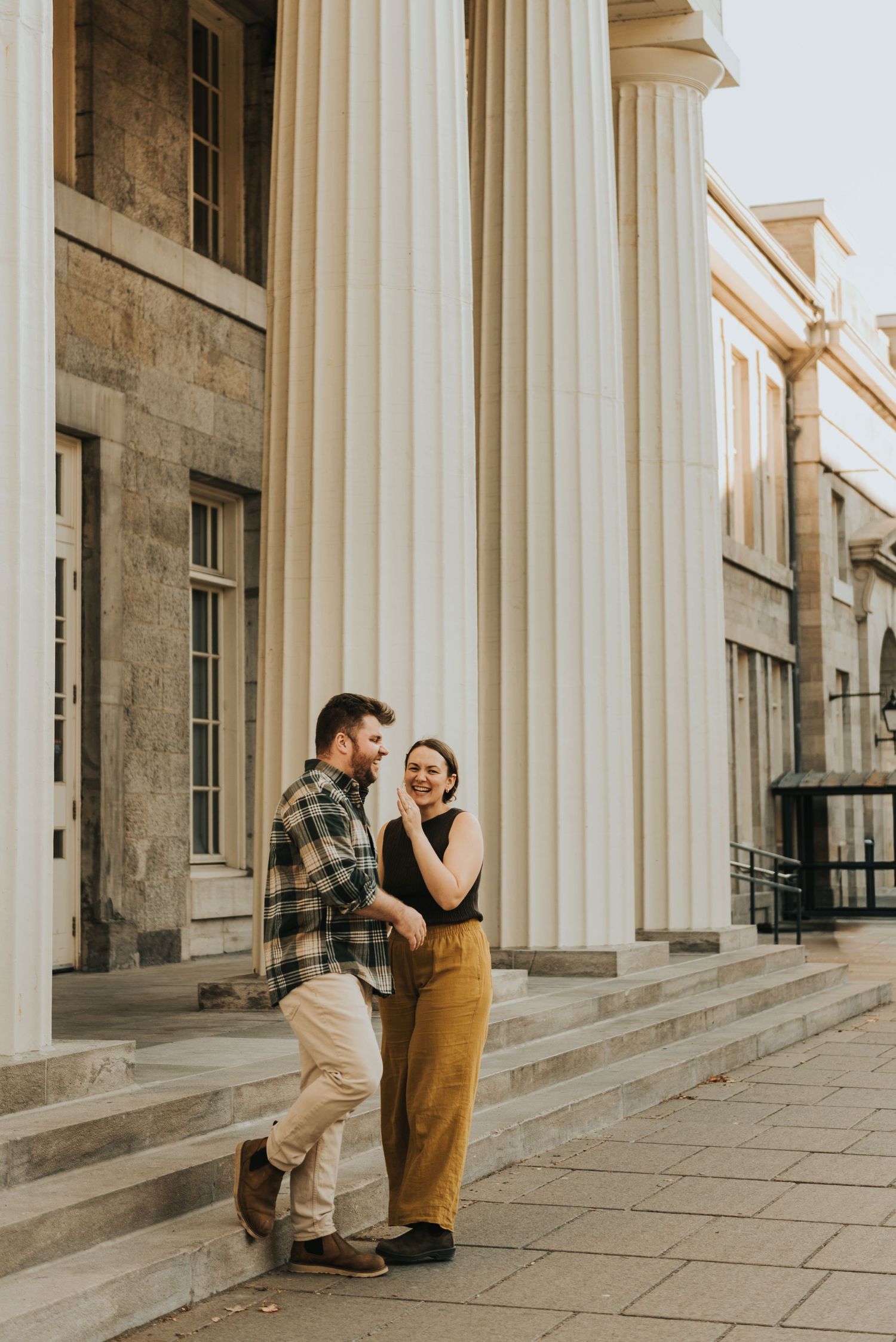 A couple shares joyful moments in front of a classical building with white columns and stone architecture.