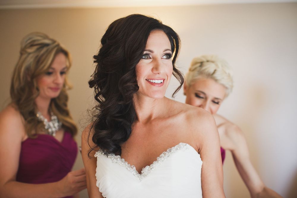 A bride in a white wedding dress gets ready with her bridesmaids in burgundy dresses during wedding preparations.