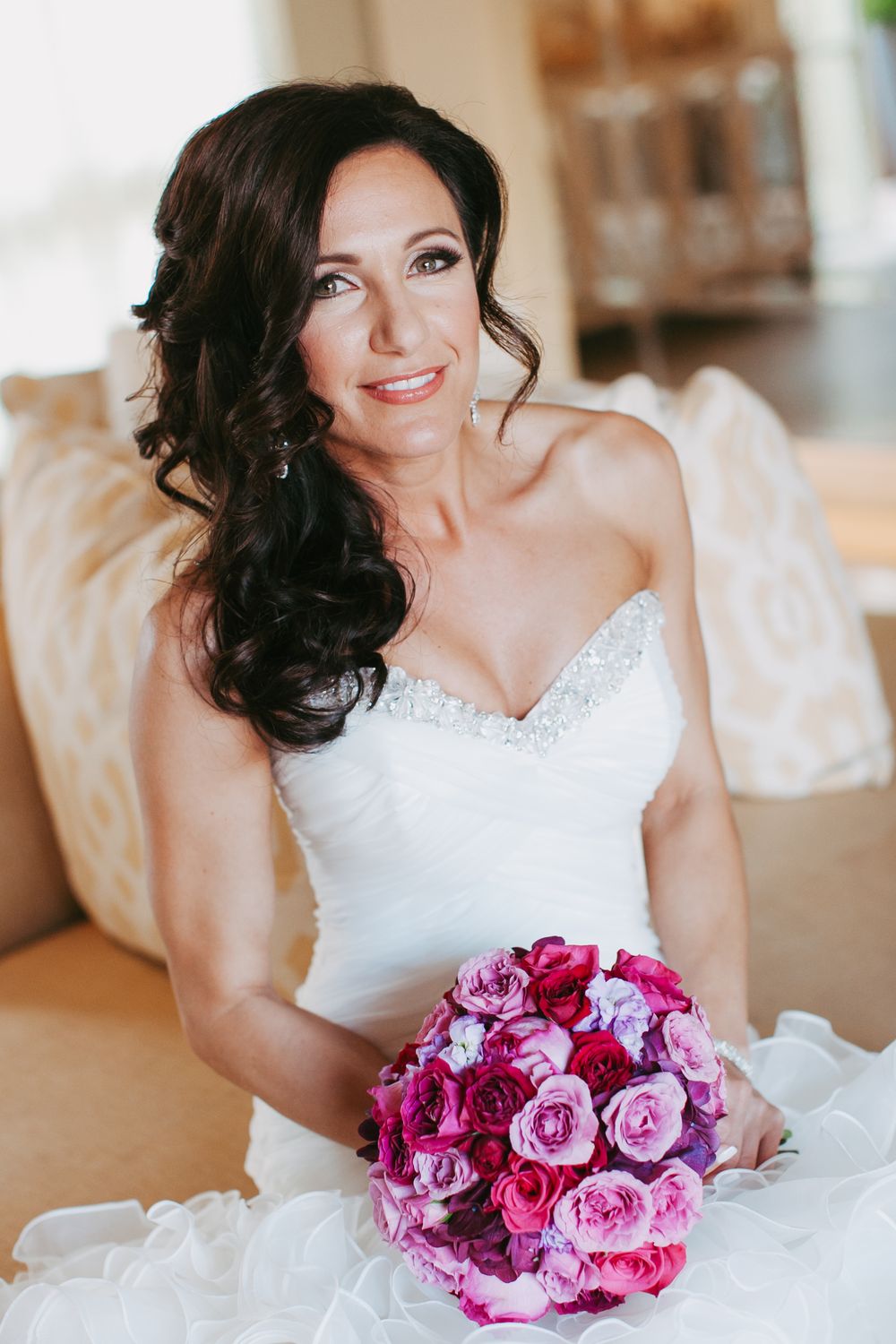 Bride in white wedding dress holding vibrant pink and fuchsia rose bouquet in elegant indoor setting.