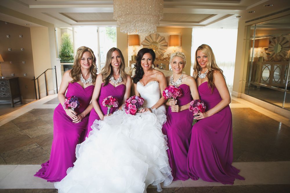 Bridal party in magenta bridesmaid dresses and white wedding gown pose together in an elegant indoor venue.