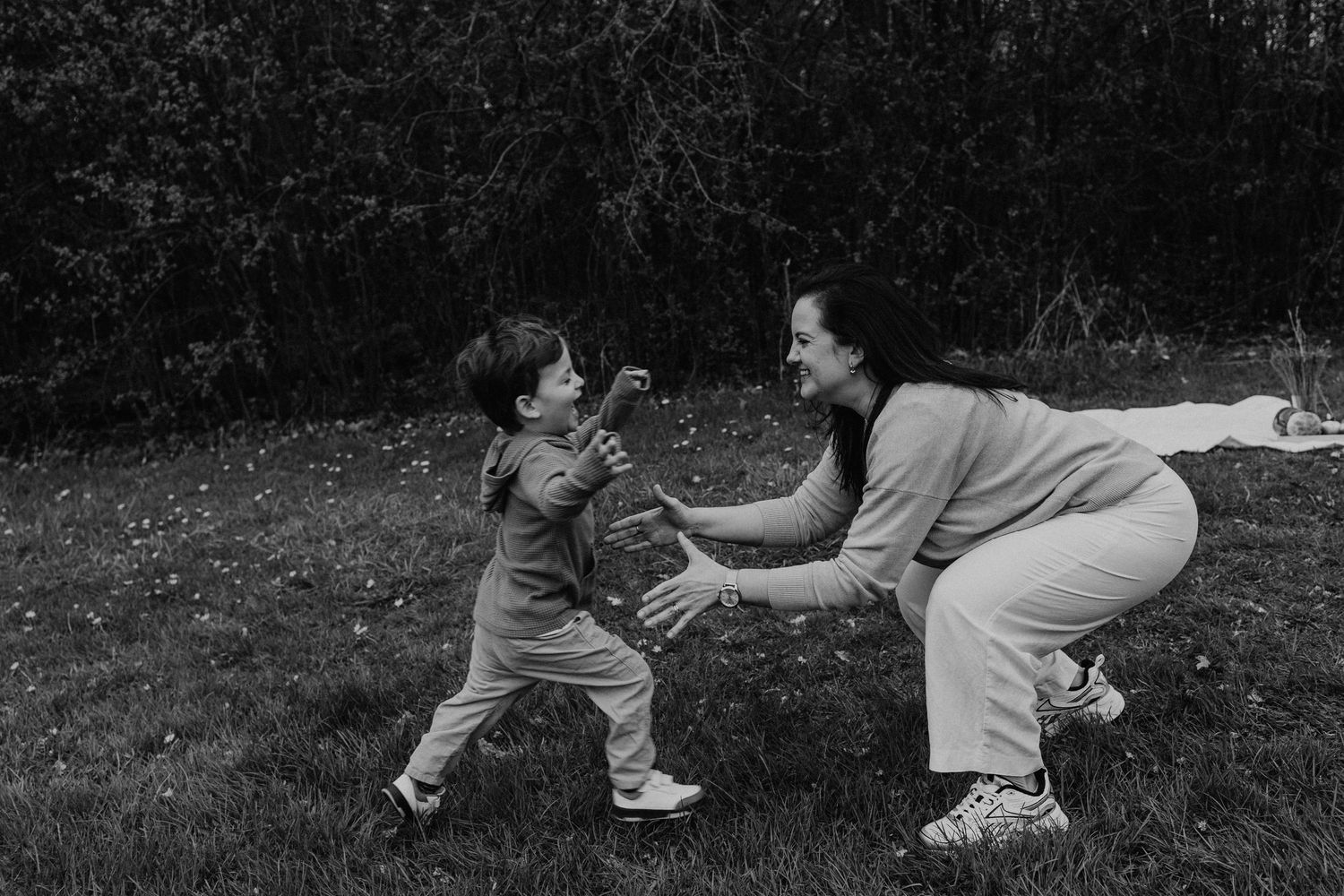 black and white photo of a son running to his mother on the park so she can lift him up